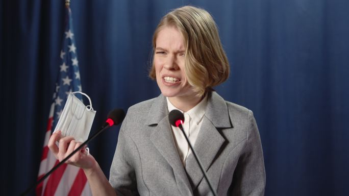 一位愤怒的白人女政治家在辩论中的演讲中手持保护性口罩