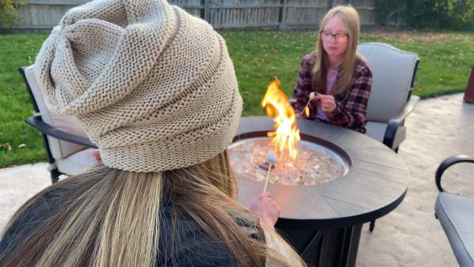 母亲和女儿坐在后院的火坑旁烤棉花糖