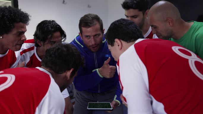 一位拉丁美洲教练一边拿着平板电脑，一边和他的足球队谈论他们的比赛策略