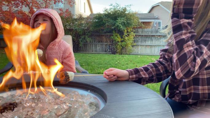 两个女孩和她们的妈妈坐在后院的篝火旁烤棉花糖