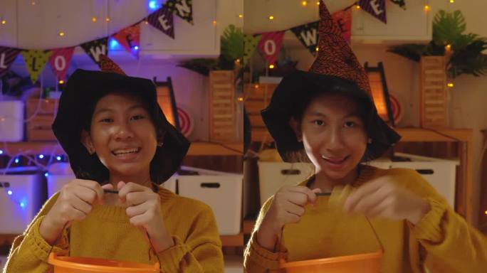一个亚洲女孩，穿着女巫的头发，手持南瓜桶，“不给糖就捣蛋”，万圣节的概念。