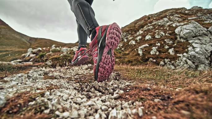 速度坡道女跑步者在散布碎石的山道上跑步的腿