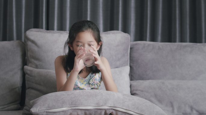 可爱的孩子在家里的客厅里用玻璃杯喝纯水
