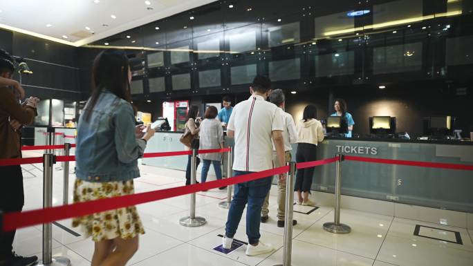 低视角亚裔中国观众在售票柜台排队购买电影票，爆米花在电影院电影放映时间前无接触支付