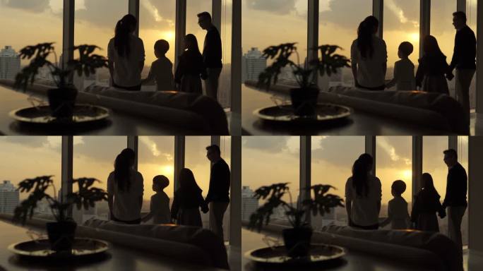 吉隆坡市起居室里，两个孩子透过窗户观看美丽的日落，侧影后视亚裔华人家庭