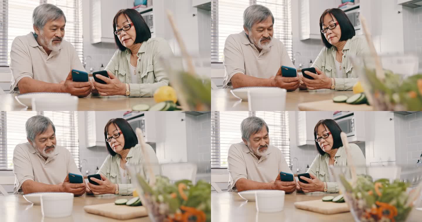 一对年长的亚洲夫妇坐在一起，在厨房里用手机。亚洲老年夫妇用手机上网、蓝牙、同步