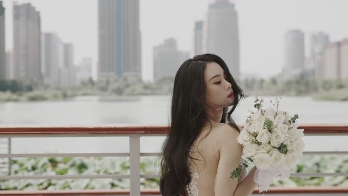 婚礼现场，一位年轻漂亮的亚洲女子穿着婚纱，手持一束鲜花，坐在遮阳伞下