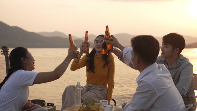 一群快乐的亚洲朋友游客在夏天在湖边露营时一起喝啤酒和快乐