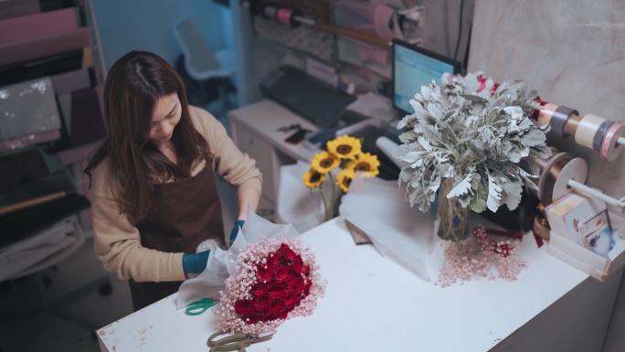 亚裔中国女花匠在她的花店柜台为顾客定购包裹红玫瑰花束