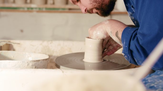 一个人的手在陶轮上模塑湿粘土。男性陶工在他的工作室里雕刻陶瓷艺术。技艺精湛的工匠，爱好爱好，制作手工