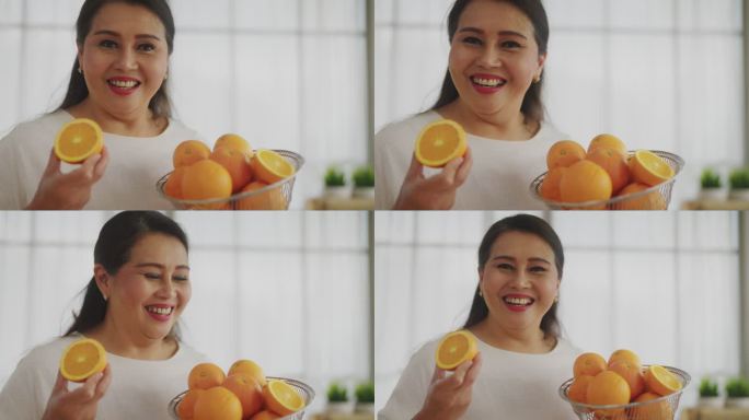 亚洲成熟女性拿着橘子片，在厨房里开心地看着摄像机