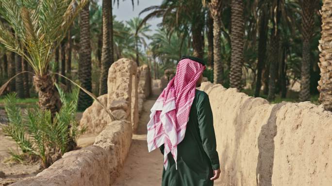 沙特男子在古老的步道上穿过沙漠绿洲