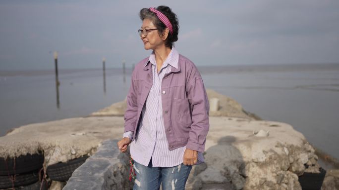 早上，亚裔中国资深女性在海滩码头微笑着看着相机散步