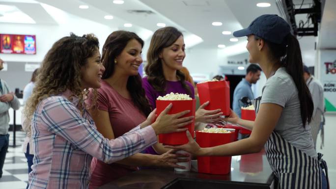 美丽的女性朋友微笑着在电影院特许店购买零食