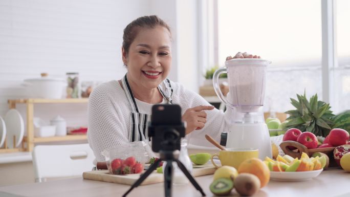 亚洲资深女性，教授如何用不同的调味品和酸奶制作自制水果冰沙。健康的天然益生菌风味饮料，学习使用技术，