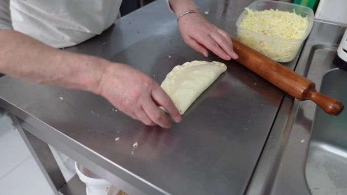 一位经验丰富的女面包师在厨房柜台上用披萨馅料制作生面团，并将其放在烤盘上的特写镜头
