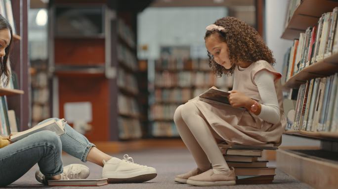 两名女性坐在图书馆的地板上一起看书。可爱的女儿和妈妈在图书馆。