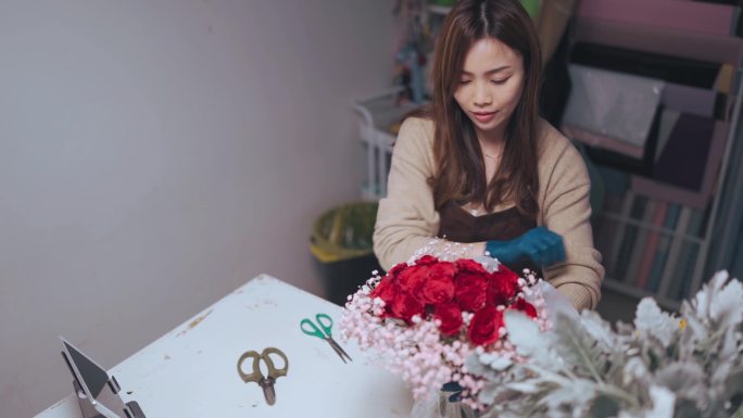亚裔中国女花匠在她的花店柜台为顾客定购包裹红玫瑰花束