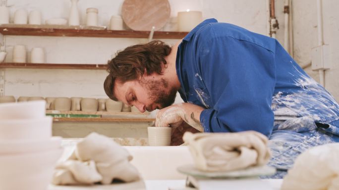 男性陶工在他的陶瓷车间里制作粘土杯。一位严肃的陶艺艺术家、雕塑家或手工艺人，在陶艺教室用双手制作手工