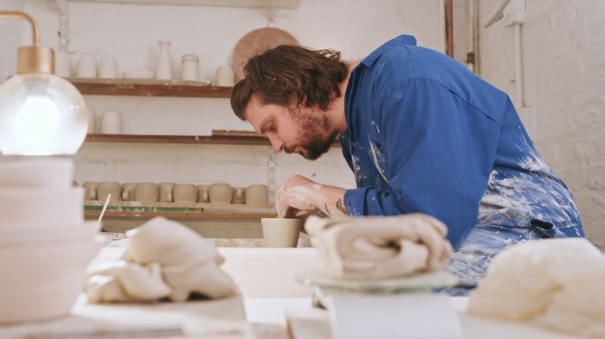 一个在陶轮上塑造湿粘土的人。男性陶工在他的工作室里雕刻陶瓷艺术。技艺精湛的工匠，爱好爱好，制作手工工