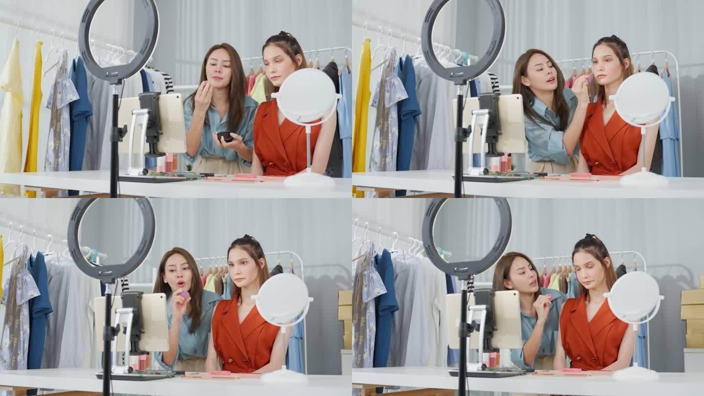 两位亚洲女性在家里对着摄像机聊天，回顾化妆品。美女博主影响力女性朋友在办公室商店的平板电脑上直播并向