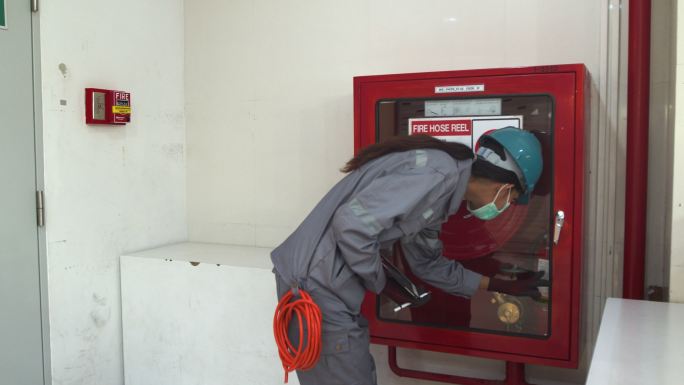 亚洲女技术员检查员检查消防水龙带轮。修复内螺纹检查报警状况