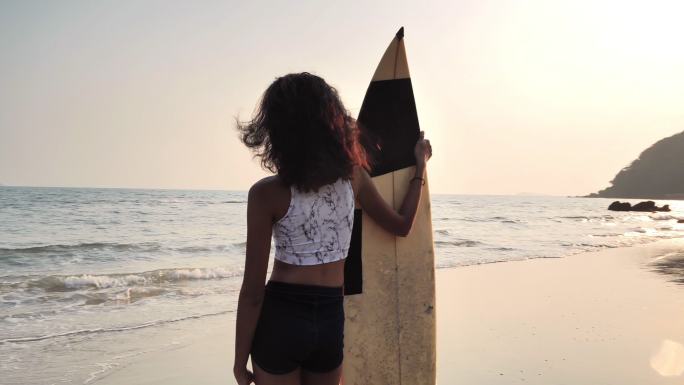 日落时沙滩上美丽性感的冲浪女孩。体育电影摄影机