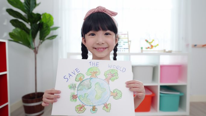 这位亚洲小学生的脸上洋溢着幸福和微笑，她正在展示并拿着自己的画作，主题是“一起拯救世界”，她画了一片