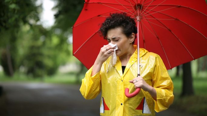 下雨天，年轻女子在公园里打喷嚏