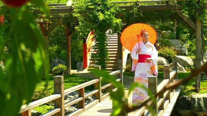 一位穿着和服、打着伞的美女沿着日本花园里的桥散步