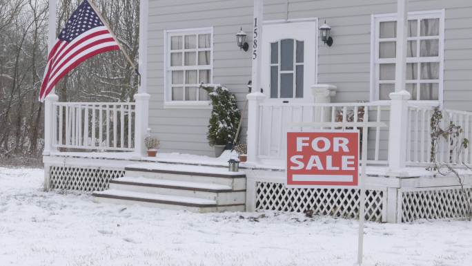 4K视频：在隆冬时节，下雪时，在宽阔的雪地覆盖的院子里，一栋大独栋房子前的房产招牌由业主出售