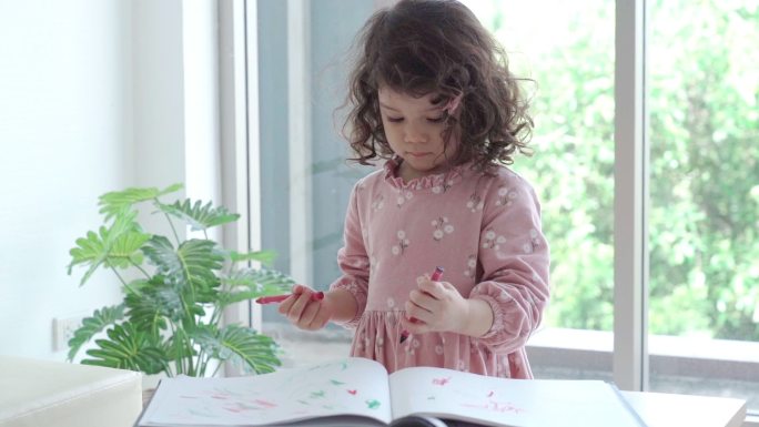 亚洲小女孩在书上用蜡笔画画，在家里的客厅里接受教育