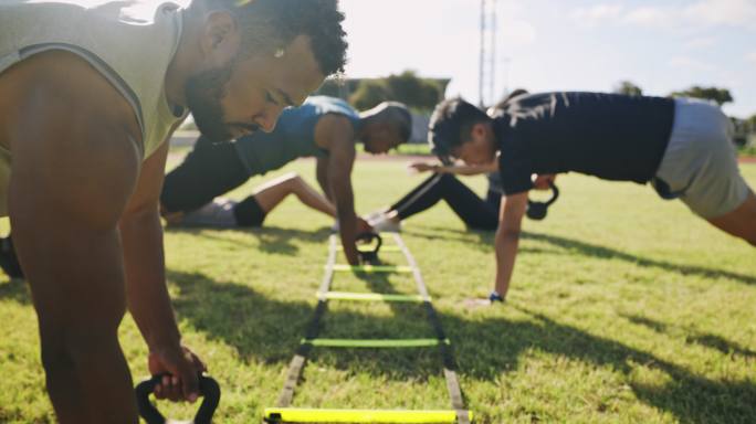 一群体格健壮、各具特色的运动人士在户外运动场上进行举重巡回训练。专门的运动员练习训练，以增加和增强肌