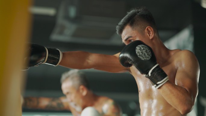 极限运动亚洲男子泰拳拳击手连续拳击沙袋在健身俱乐部一起练习