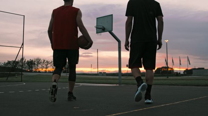 中景：黄昏时分，年轻人走出室外篮球场。两个朋友在户外篮球场散步。