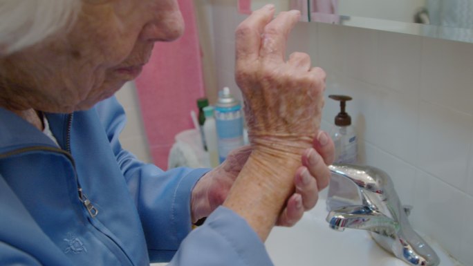 一位100岁的老人在浴室水槽上用手擦润肤乳液