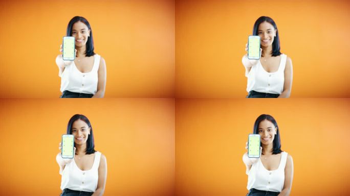 一名年轻女性在橙色工作室背景下展示绿色屏幕智能手机的4k视频片段