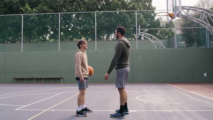 父子俩正在打篮球。年轻人和十几岁的男孩玩得很开心，在保持健康的同时打了一拳，很活跃
