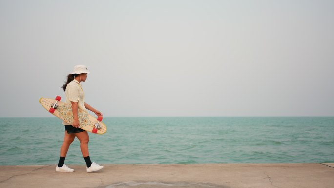 手拿滑板的女人在海边散步
