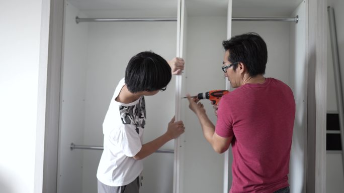 亚裔青少年正在帮助父亲在家中安装木制橱柜。