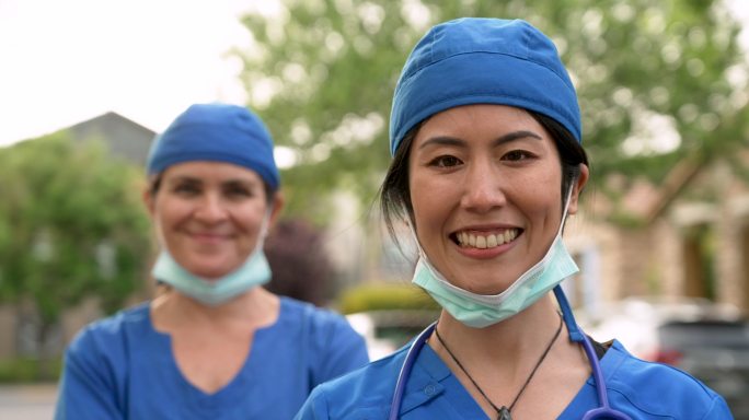 微笑的亚裔和高加索医护人员戴着防护面罩
