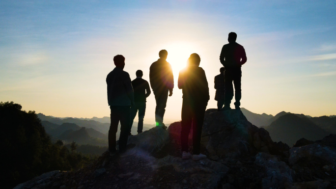 团队登山攀登顶峰一群人山顶逆光剪影看日落