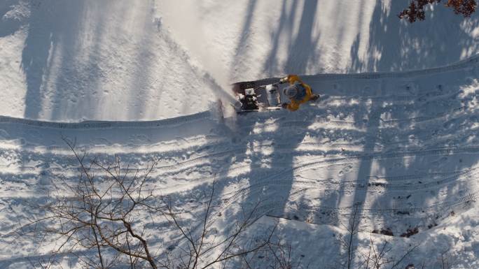 冬季降雪后，一名成年男子用吹雪机清理车道上的积雪。无人机视频正上方的鸟瞰图。