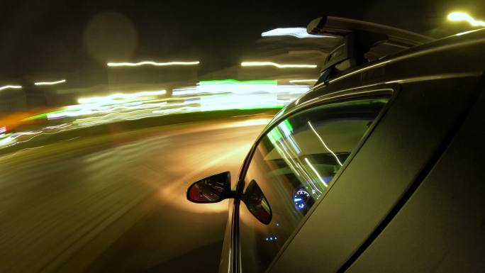 夜间驾车快速行驶。汽车行驶。时间流逝。侧镜、侧门和车窗中的城市反射光。