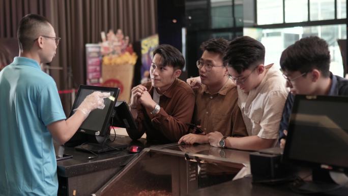 亚裔中国年轻男子在电影院电影放映时间前，在酒吧柜台用非接触式支付方式点了爆米花