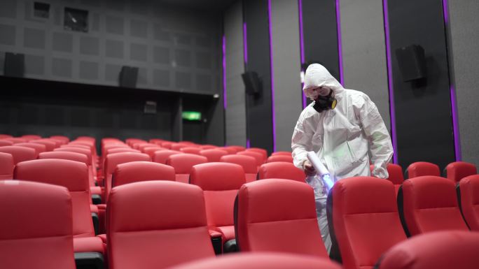 电影放映前，戴着口罩的亚裔中国电影院卫生员在电影院大厅的椅子和地毯上进行消毒