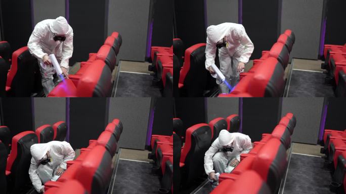 电影放映前，戴着口罩的亚裔中国电影院卫生员在电影院大厅的椅子和地毯上进行消毒