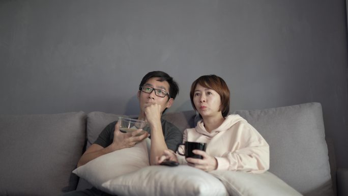 坐在沙发上看电视电影的亚裔中国夫妇。