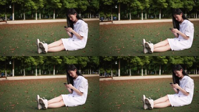 白衣长发年轻美女坐草地上看手机微笑开心