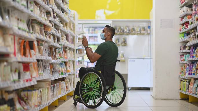 周末，亚裔印度残疾男子坐轮椅在超市购物，用智能手机查看购物清单
